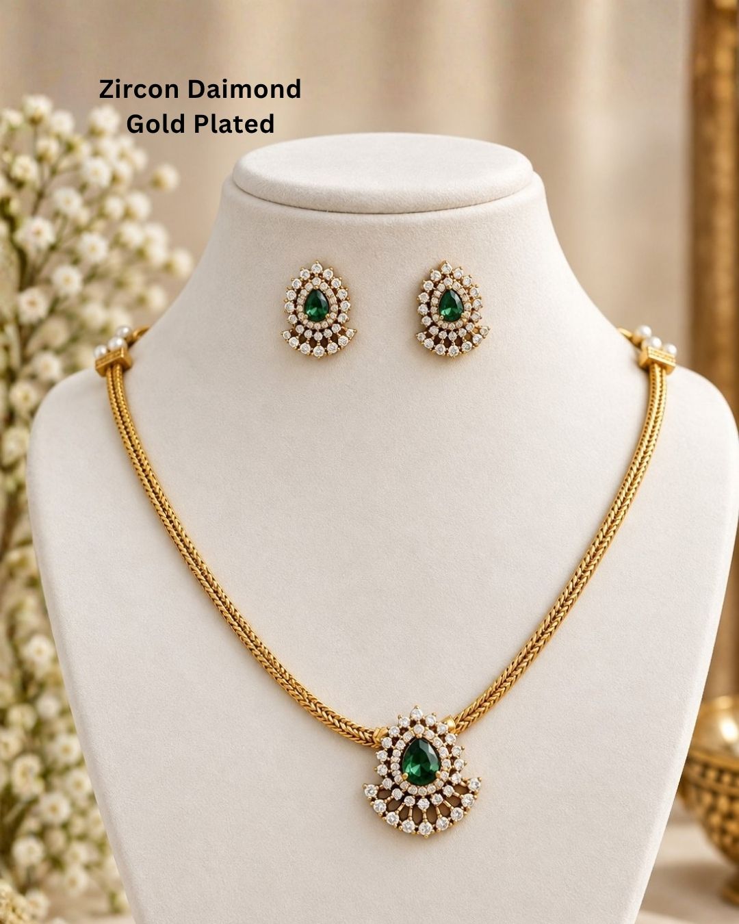 A minimalist 18k gold plated herringbone chain necklace featuring a central teardrop-shaped ruby green stone. The stone is enclosed in a halo of white pure Zircon diamonds that flares out at the bottom into a shimmering, fan-shaped scalloped fringe, paired with matching crown-set ear studs.