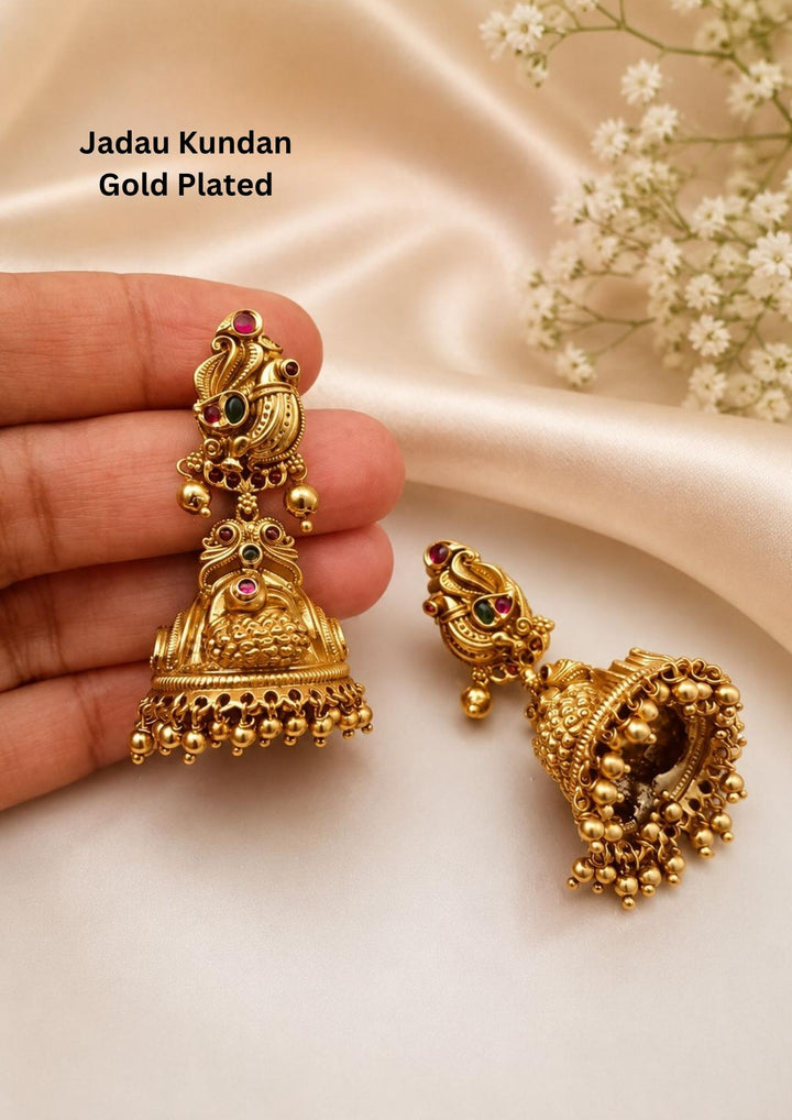 Gold plated Jadau Kundan jhumka earrings designed with peacock top stud decorated with small ruby pink and emerald green stone accents. The traditional antique dome-shaped jhumki base is crafted with Nakshi floral engravings, dainty colored stone highlights, and finished with a dense, multi-layered of hanging gold beads suitable for family gatherings, festivals, parties, and weddings with skin friendly