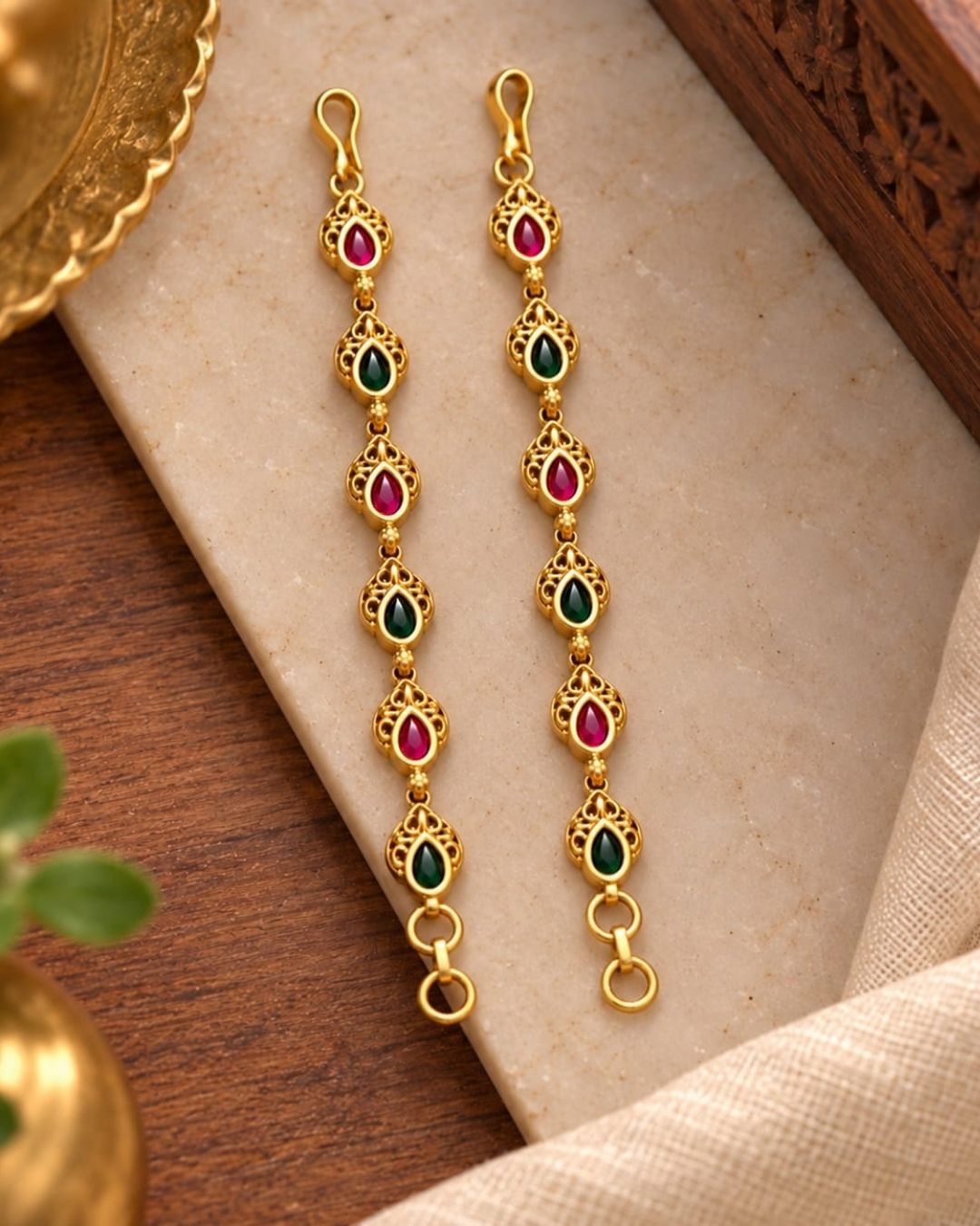 Gold plated traditional ear chains featuring alternating red and green teardrop stones with intricate antique gold detailing.