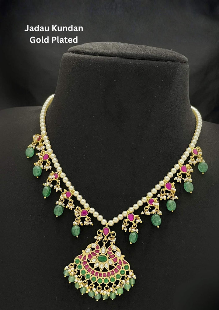 A traditional 18k gold plated haram necklace featuring a single strand of elegant white pearls. The lower half is accentuated with hanging ruby-pink and emerald-green stone links that culminate in a large, fan-shaped central pendant intricately inlaid with colorful gemstones, finished with a fringe of dangling green beads and tiny pearl clusters, perfect for weddings, bridal wear, receptions, office and it comes with anti tarnish , anti color fade and skin friendly