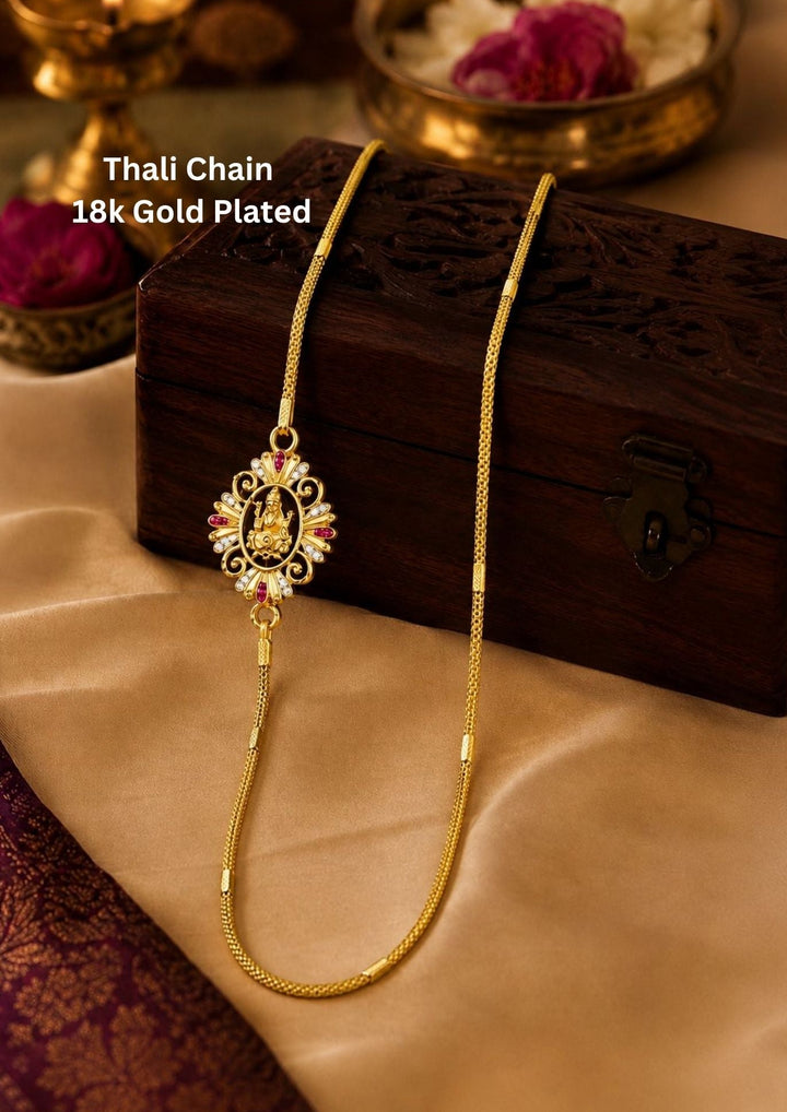 gold plated thali chain featuring a beautifully crafted central Goddess Lakshmi mogappu side pendant embellished with sparkling white zircon stones and ruby pink gemstone accents. This high-quality classic woven chain design mimics a premium gold wedding chain, providing a rich and traditional appearance suitable for weddings, festivals, poojas, daily wear, family functions, traditional sarees, and ethnic outfits with skin-friendly quality, anti-fade long-lasting polish, comfortable weight
