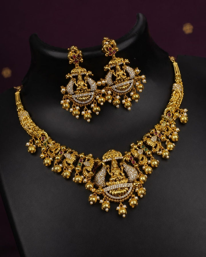 Elegant gold plated bridal temple necklace and earrings set adorned with Goddess Lakshmi motifs, shimmering CZ stones, pearl hangings, and intricate handcrafted detailing.
