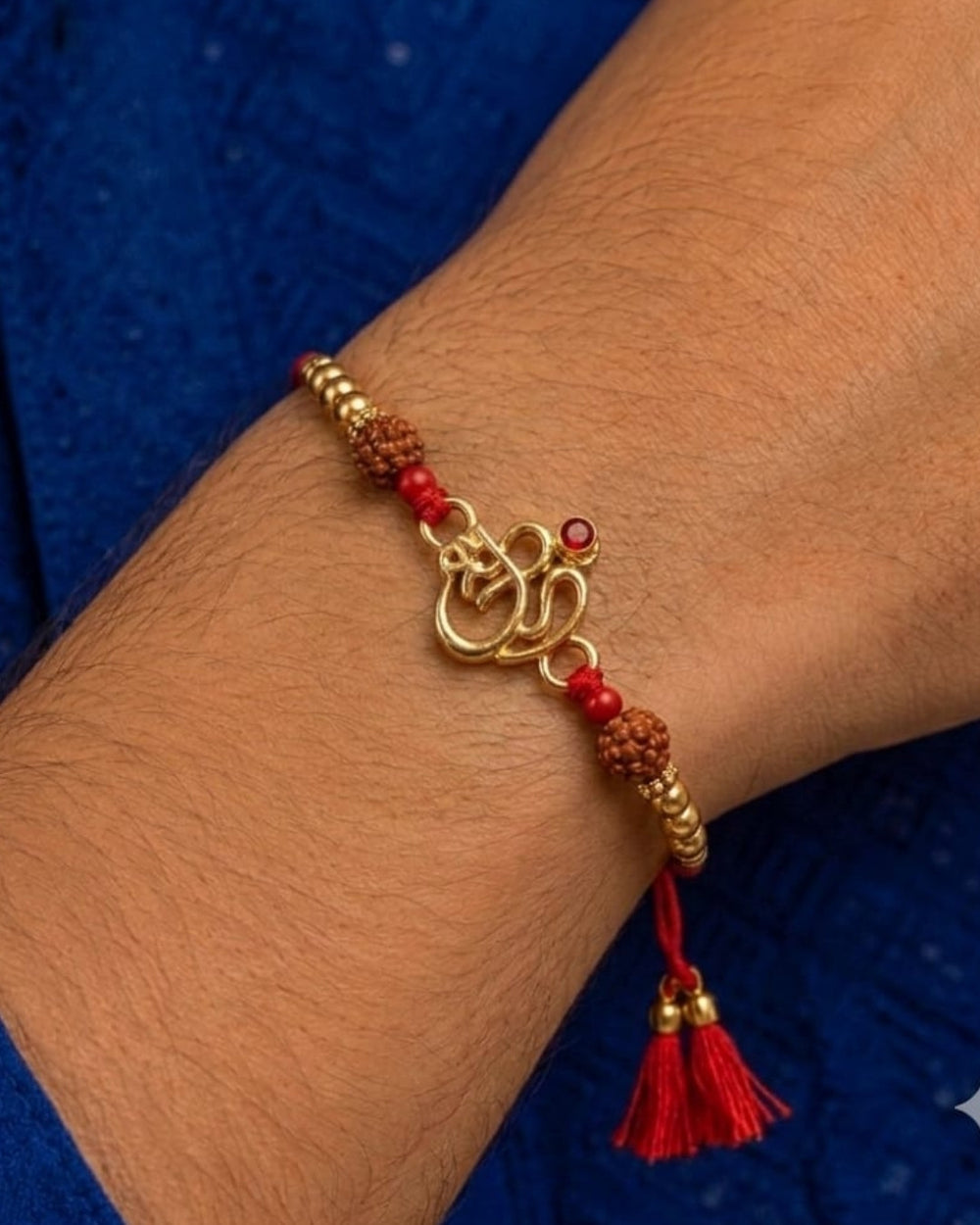 Elegant spiritual Rakhi showcasing a gold plated Om motif accented with a red stone, Rudraksha beads, and decorative gold beads on a red thread.