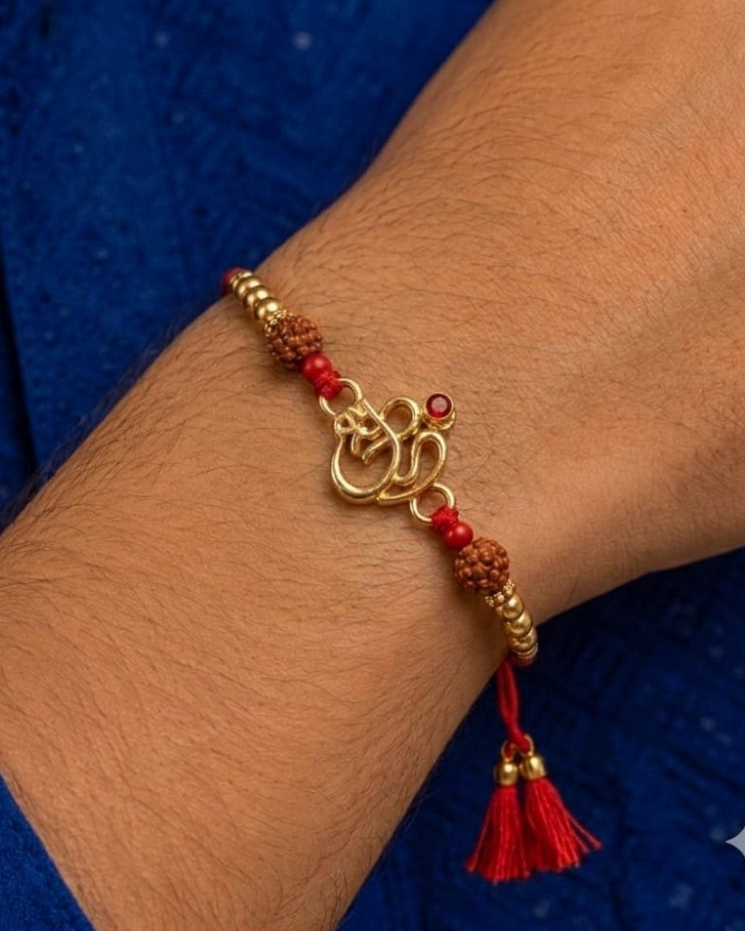 Elegant spiritual Rakhi showcasing a gold plated Om motif accented with a red stone, Rudraksha beads, and decorative gold beads on a red thread.