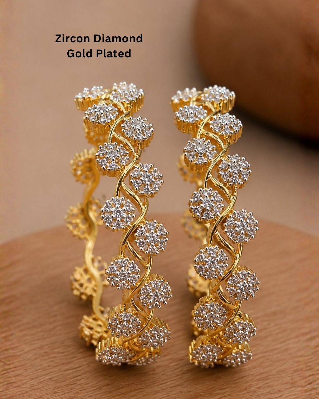 A pair of gold-plated huggie bangles decorated with clear zircon stones in a floral pattern, displayed on a wooden surface with a warm brown background. Text overlay reads 'Zircon Diamond Gold Plated'.