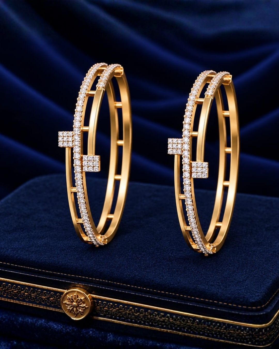 Pair of gold plated crystal bangles displayed on a navy blue jewellery box with a luxurious dark blue background.