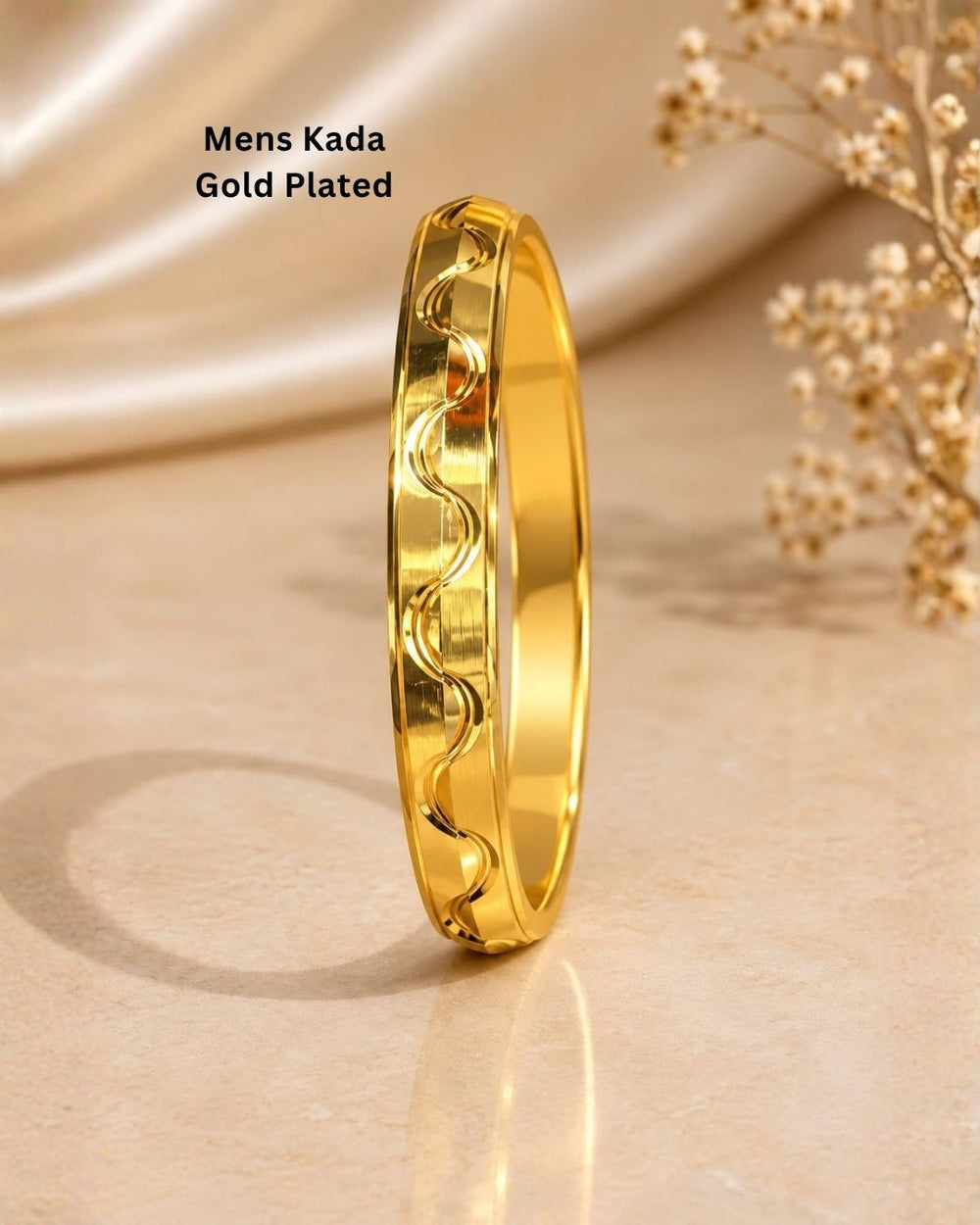 Gold plated men’s kada displayed upright on a beige surface, showcasing its modern wave pattern and reflective finish.