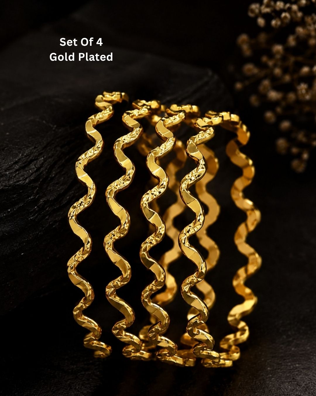 Four gold-plated spiral bangles displayed together on a dark textured surface, with white text in the upper left reading 'Set Of 4 Gold Plated'.