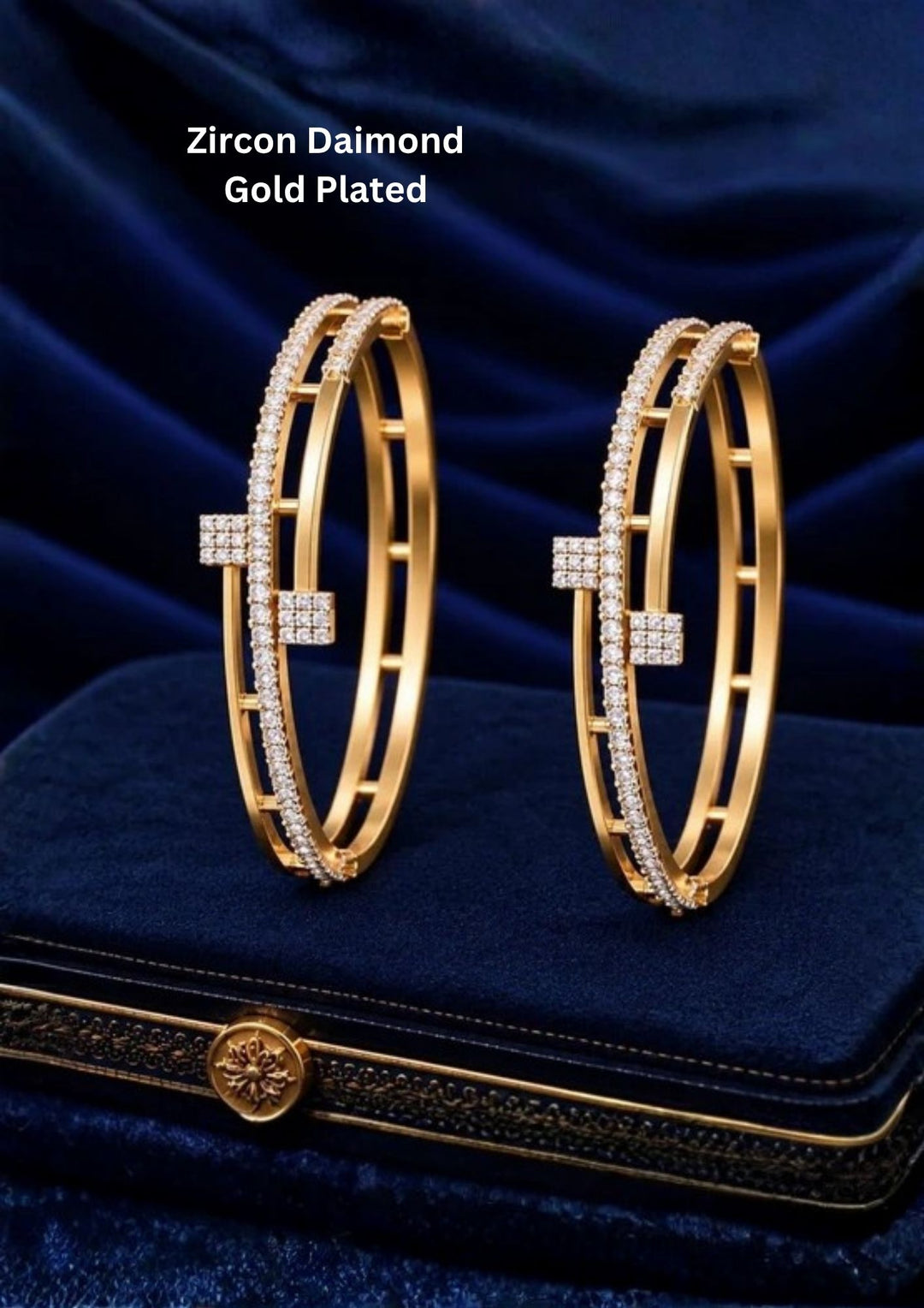 Pair of gold plated crystal bangles displayed on a navy blue jewellery box with a luxurious dark blue background.