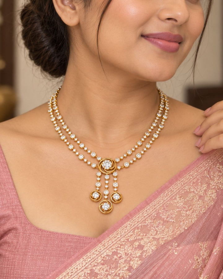Gold plated two-layer necklace and matching hanging earrings set featuring two lines of small, round white stones. The chains join at a central round flower motif, from which three delicate lines of white stones hang down, each ending in a small circle design. The set features a clean layout suitable for festivals, family parties, and traditional celebrations.