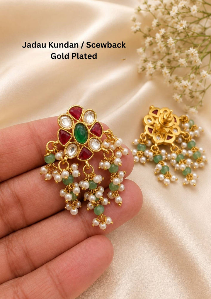 Gold plated Jadau Kundan stud earrings deisgned in flower-shaped top design with an oval green emerald center stone surrounded by alternating teardrop-shaped white kundan crystals and ruby red gemstones. The lower section of the earrings is designed with guttapusalu   suitable for family gatherings, festivals, parties, and weddings with skin friendly quality, anti fade color