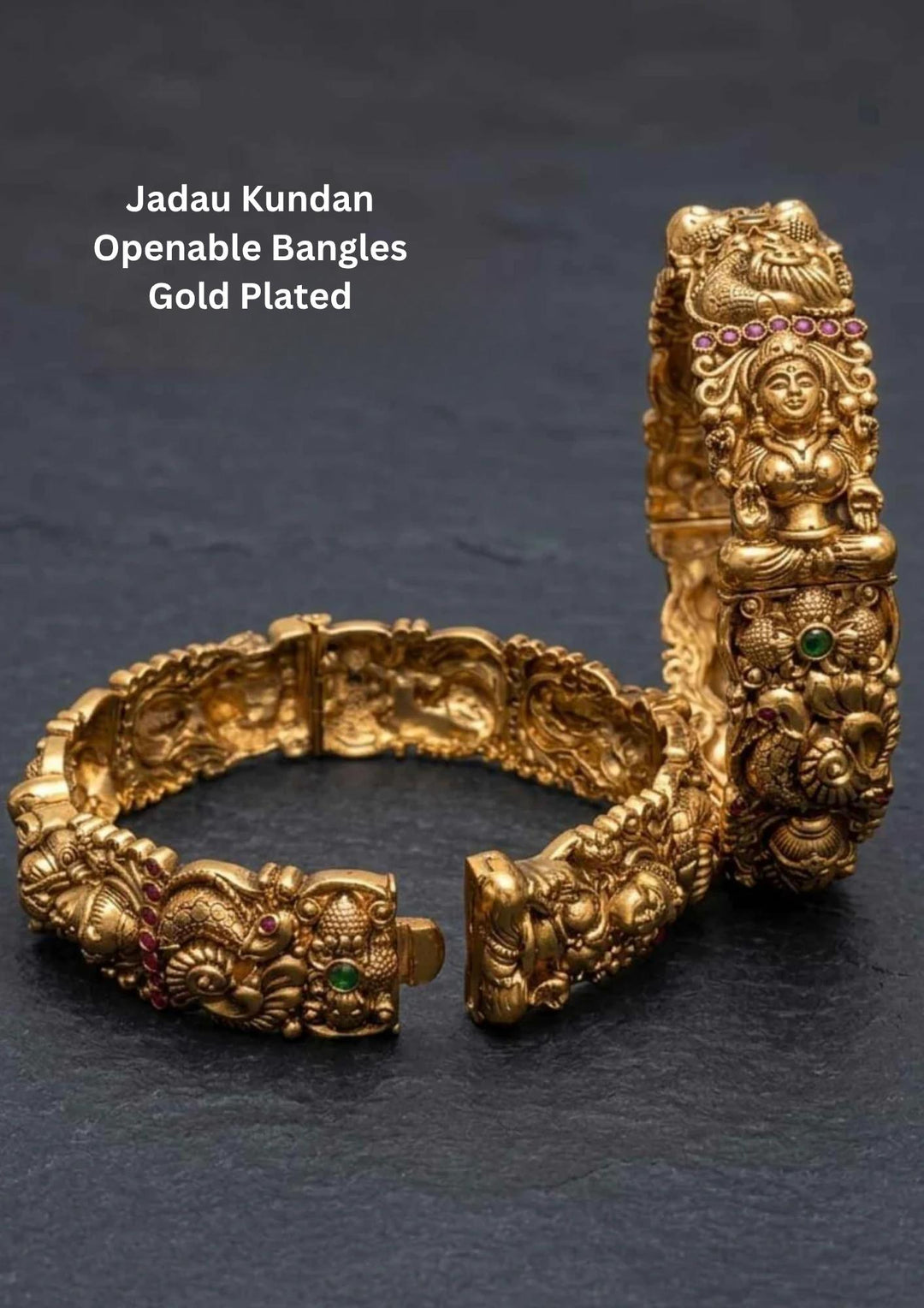 A pair of heavy, antique gold plated openable temple kadas featuring deeply embossed high-relief panels of Goddess Lakshmi seated on a lotus throne. The traditional bands are detailed with intricate floral scrollwork, pink rubies, a green emerald core accent, and a secure push-plug hinged clasp.