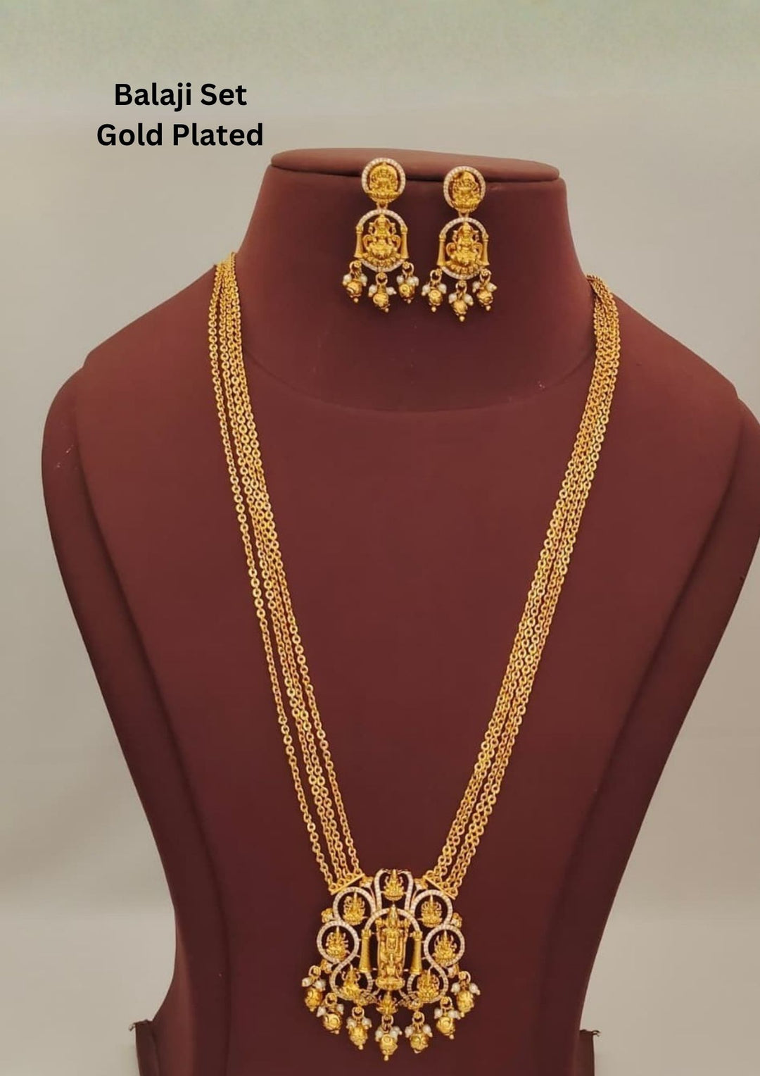 Premium gold plated temple long haram featuring a grand Lakshmi pendant, four-layer chain design, intricate temple motifs, pearl drops, and matching Lakshmi earrings for traditional occasions.