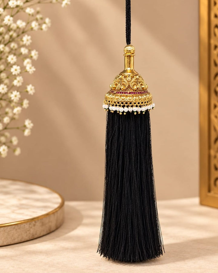 Elegant gold plated Jada Gantalu with intricate temple-inspired craftsmanship, ruby stone accents, pearl detailing, and long black tassels, perfect for bridal and festive hairstyles.
