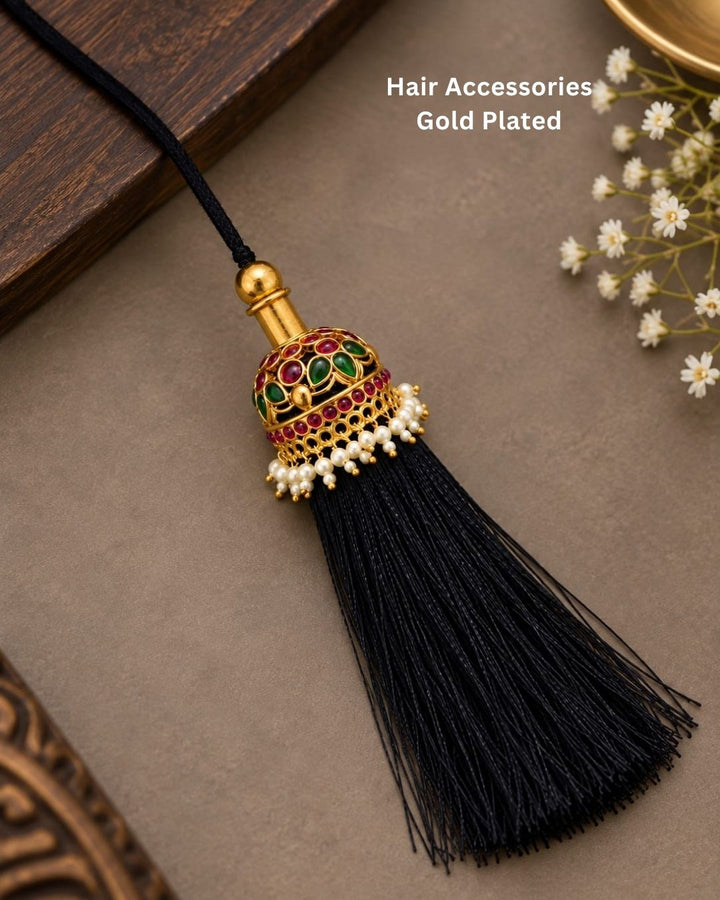 Elegant gold plated Jada Gantalu with intricate dome-shaped detailing, green and ruby stones, pearl accents, and long black thread tassels, perfect for bridal and festive hairstyles.