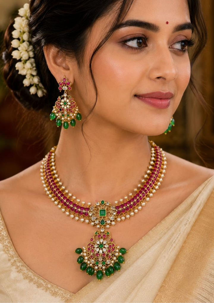 South Indian woman styling a jadau kundan gold plated choker necklace set with matching earrings. The jewelry features rich ruby stones, classic kundan work, elegant pearl detailing and emerald green bead danglers that beautifully complement silk sarees, bridal wear, lehengas and traditional ethnic outfits.