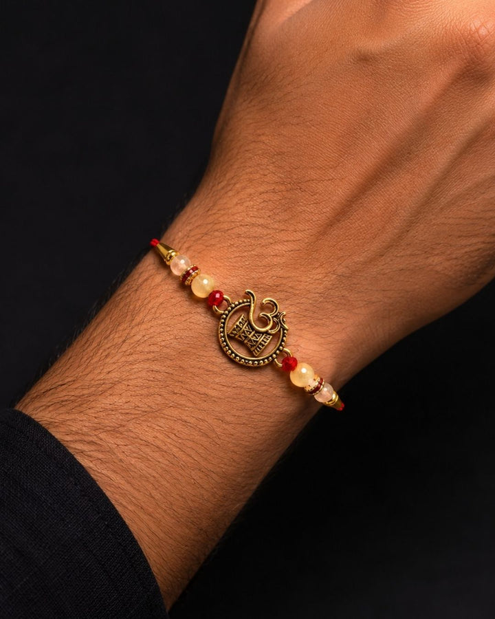 A gold-plated Swastika symbol charm bracelet with red and cream beads, shown worn on a person&