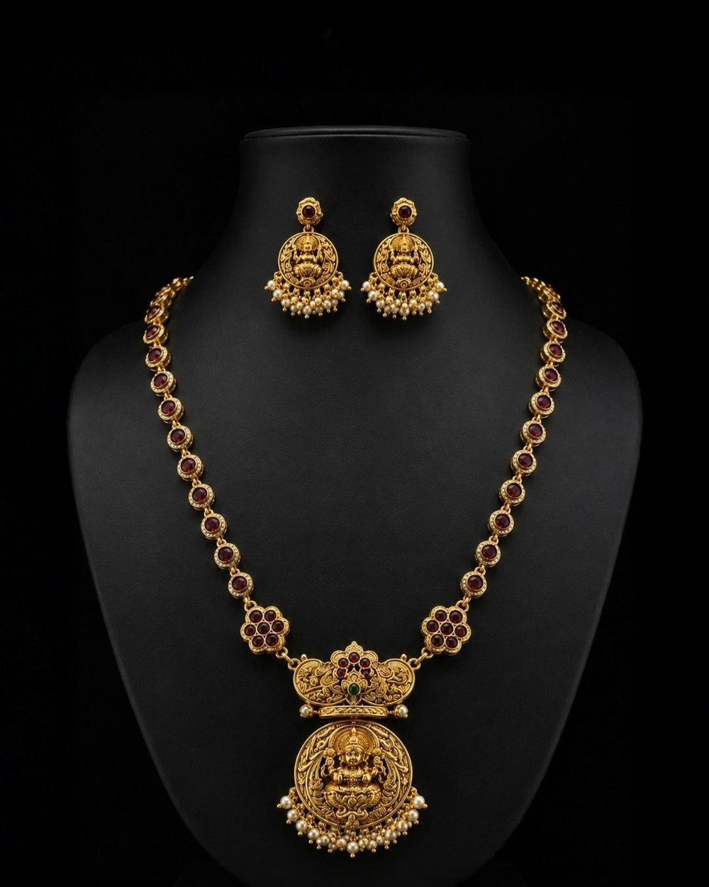 Premium gold plated CZ jewelry set with a ruby stone necklace, floral pendant, emerald green accents, pearl embellishments, and matching earrings for weddings and parties.