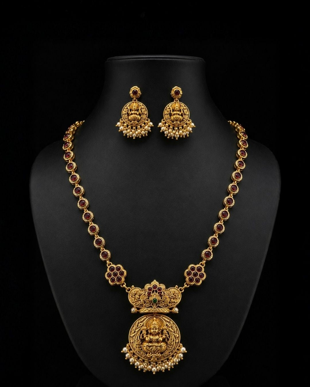 Premium gold plated CZ jewelry set with a ruby stone necklace, floral pendant, emerald green accents, pearl embellishments, and matching earrings for weddings and parties.