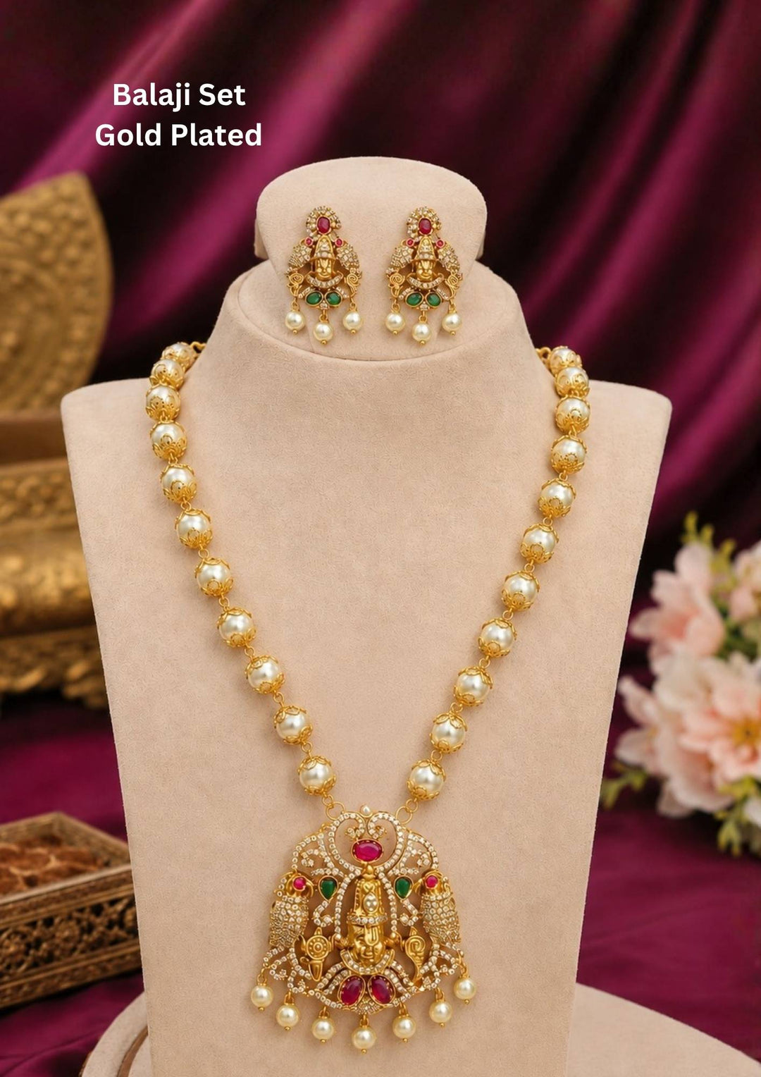 A traditional South Indian Balaji set gold plated long necklace. The piece consists of a string of round golden-capped faux pearls leading to a large, intricately detailed Lord Venkateswara pendant embellished with ruby red and emerald green stones, accompanied by matching deity earrings.