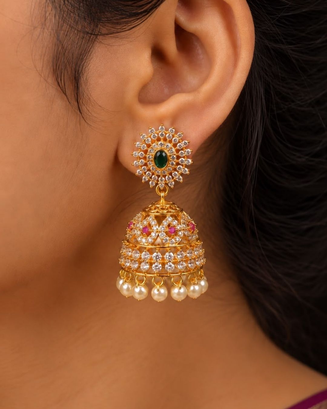 Beautiful gold plated designer jhumka earrings featuring intricate floral detailing, green stones, pink and white stone accents, and a row of elegant pearl drops. Perfect for festive occasions, traditional wear, weddings, and gifting.