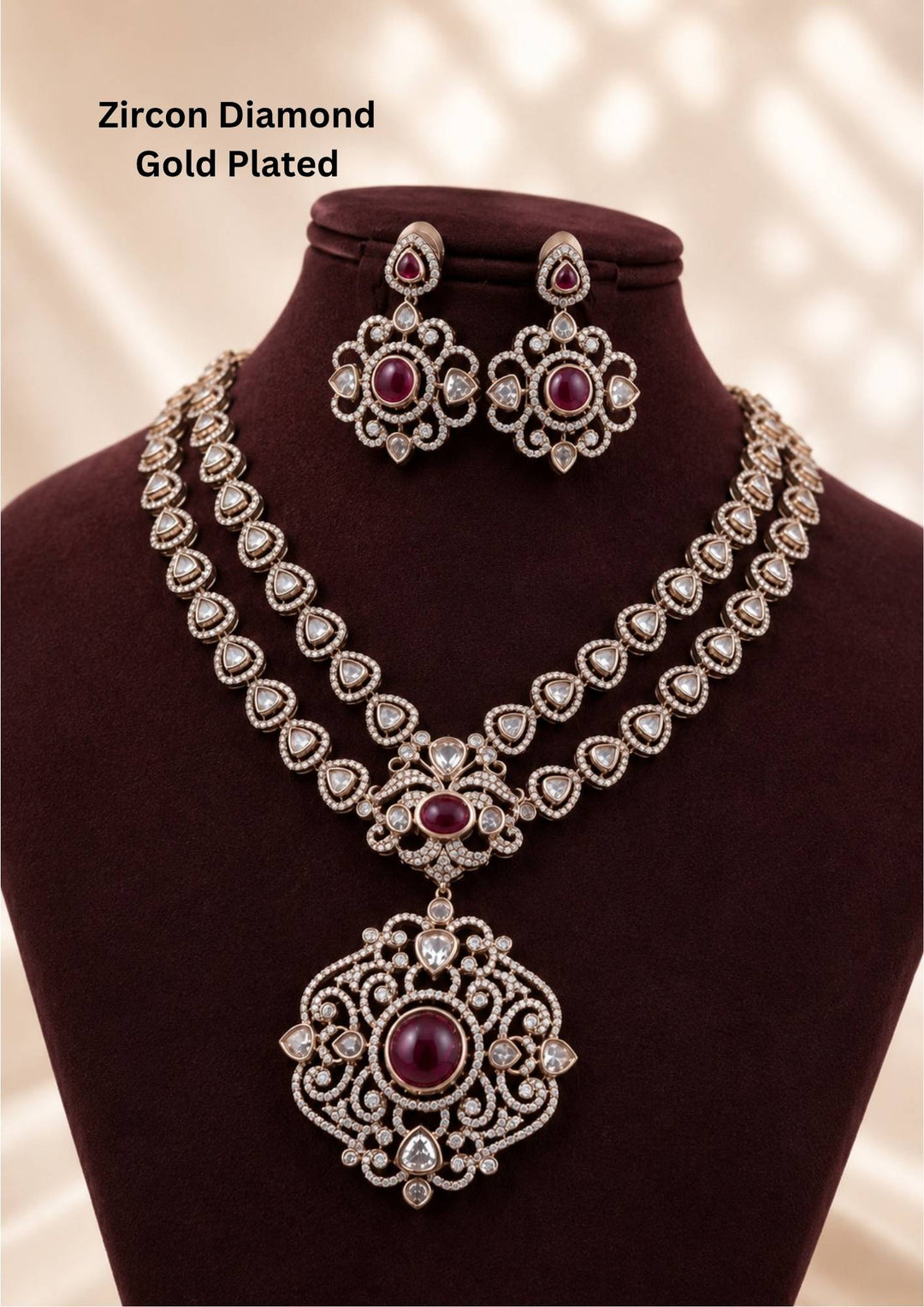 gold plated jewelry set featuring a double-layered chain of triangular trim motifs studded with pure zirconian diamonds, connected to a large, intricate filigree medallion pendant with a prominent round magenta ruby stone centerpiece. The matching large hanging earrings echo the same ornate floral pattern with a center ruby accent. Perfect for weddings, festivals, receptions, and grand family functions with skin-friendly quality, comfortable fitting