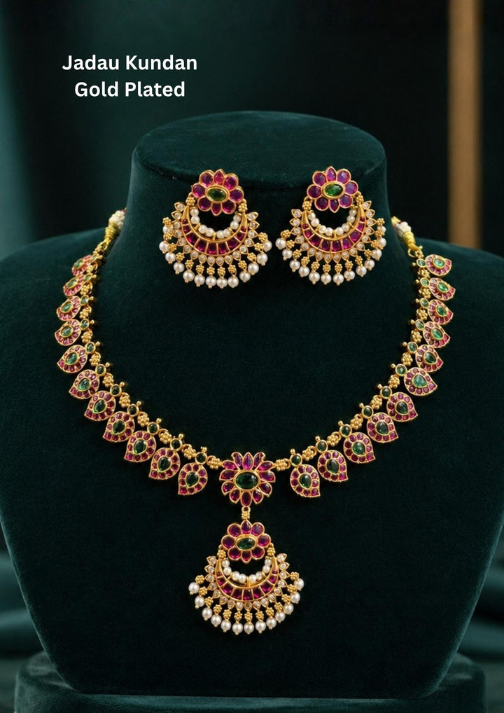 Traditional jadau kundan gold plated necklace set featuring intricate floral motifs adorned with vibrant pink and green stones along with elegant pearl drops. The matching statement earrings enhance the ethnic charm, creating a luxurious and festive jewelry design perfect for weddings and traditional celebrations.