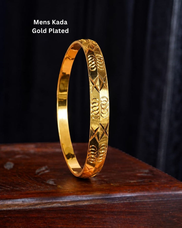Gold plated men’s kada displayed upright on a dark wooden surface against a black background, highlighting its intricate geometric detailing.