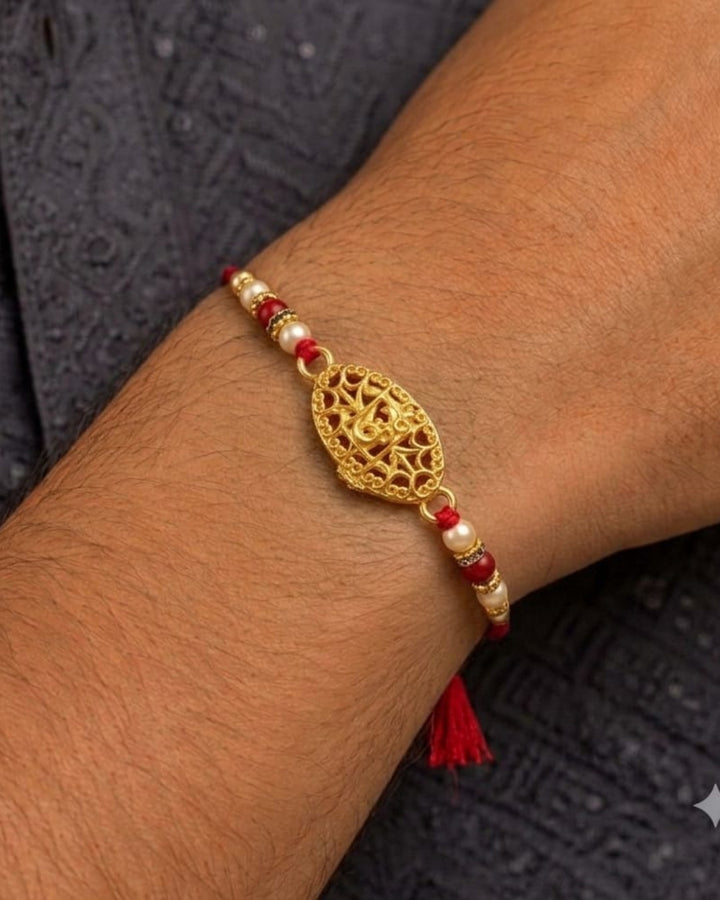 Elegant gold plated Rakhi showcasing a detailed Om symbol centerpiece with decorative pearl and red bead embellishments on a vibrant red thread.