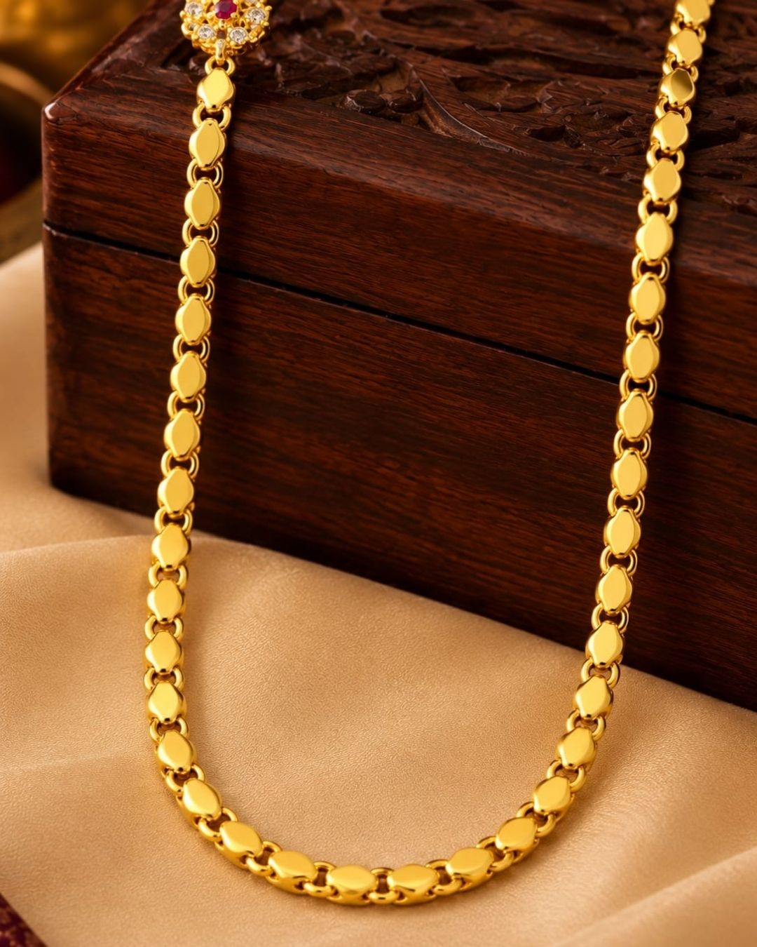 Designer gold plated thalli chain displayed on beige silk with a carved wooden jewellery box, featuring a round ruby stone centre design and matching ornamental accents.