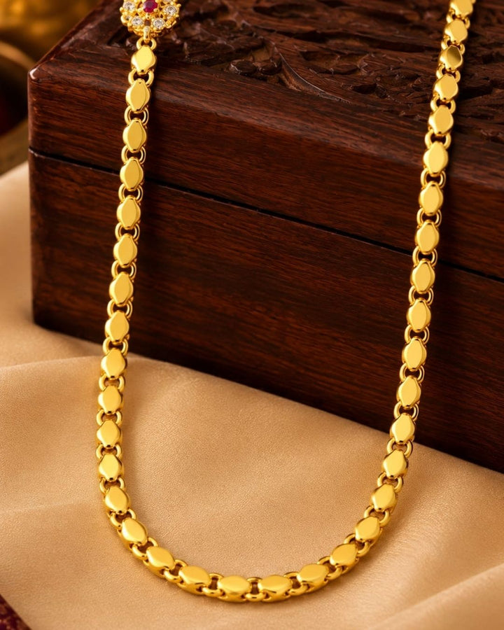 Designer gold plated thalli chain displayed on beige silk with a carved wooden jewellery box, featuring a round ruby stone centre design and matching ornamental accents.