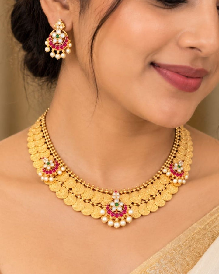 Traditional gold plated designer necklace and earrings set featuring rows of detailed coin motifs, floral designs with ruby, green and white stones, and pearl drops, perfect for festive, wedding, and traditional occasions.
