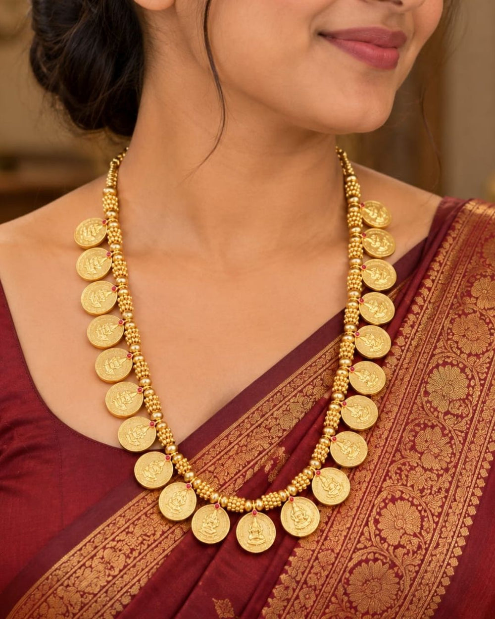 Traditional gold plated designer necklace featuring multiple Goddess Lakshmi coin motifs arranged along a detailed beaded chain, accented with small ruby-colored stones, perfect for festive, wedding, and traditional occasions.