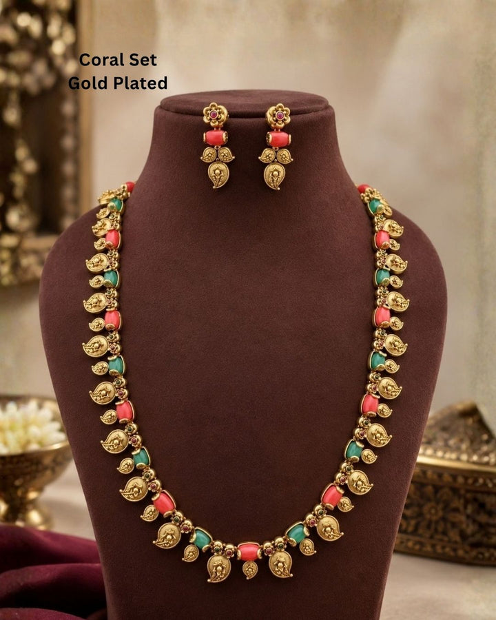 Elegant gold plated coral temple jewellery set featuring detailed traditional motifs, coral-colored and green stone embellishments, and matching earrings, perfect for festive and ethnic wear.