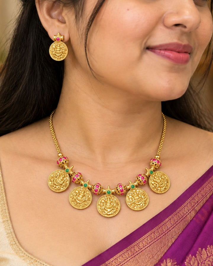 Traditional gold plated designer necklace and earrings set featuring multiple Goddess Lakshmi coin pendants, intricate temple-inspired detailing, ruby and green stone accents, and matching Lakshmi coin earrings, perfect for festive, wedding, and traditional occasions.