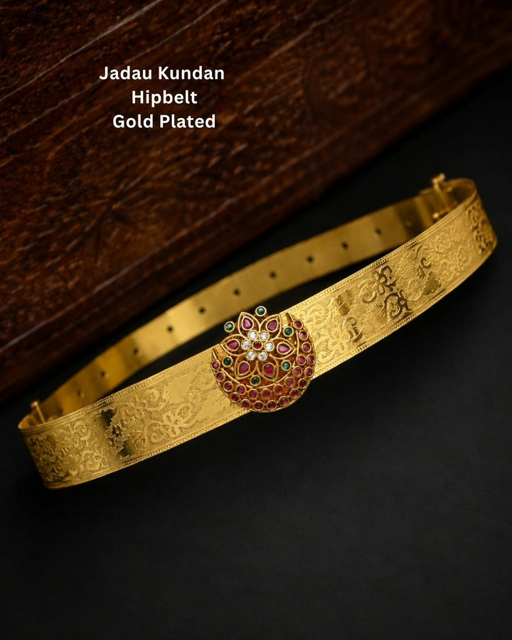 Beautiful gold plated hip belt featuring an intricately engraved wide band with a floral gemstone centerpiece accented with ruby, green, and white stones. Perfect for traditional wear, weddings, festive occasions, bridal styling, parties, and gifting.