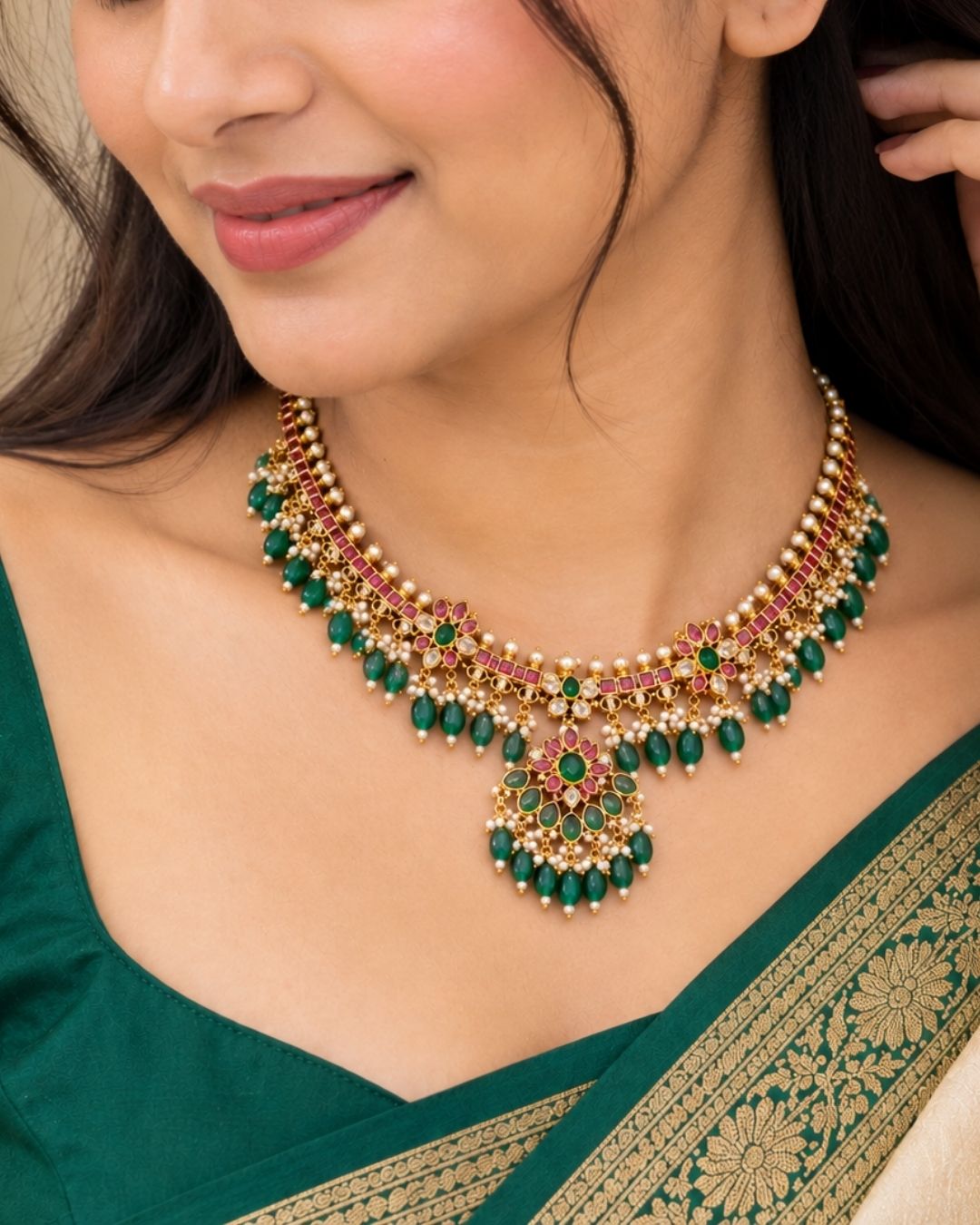 Traditional gold plated designer necklace and earrings set featuring intricate floral motifs with green and ruby-colored stones, sparkling white stones, pearl embellishments, and multiple green bead drops, perfect for festive, wedding, and traditional occasions.