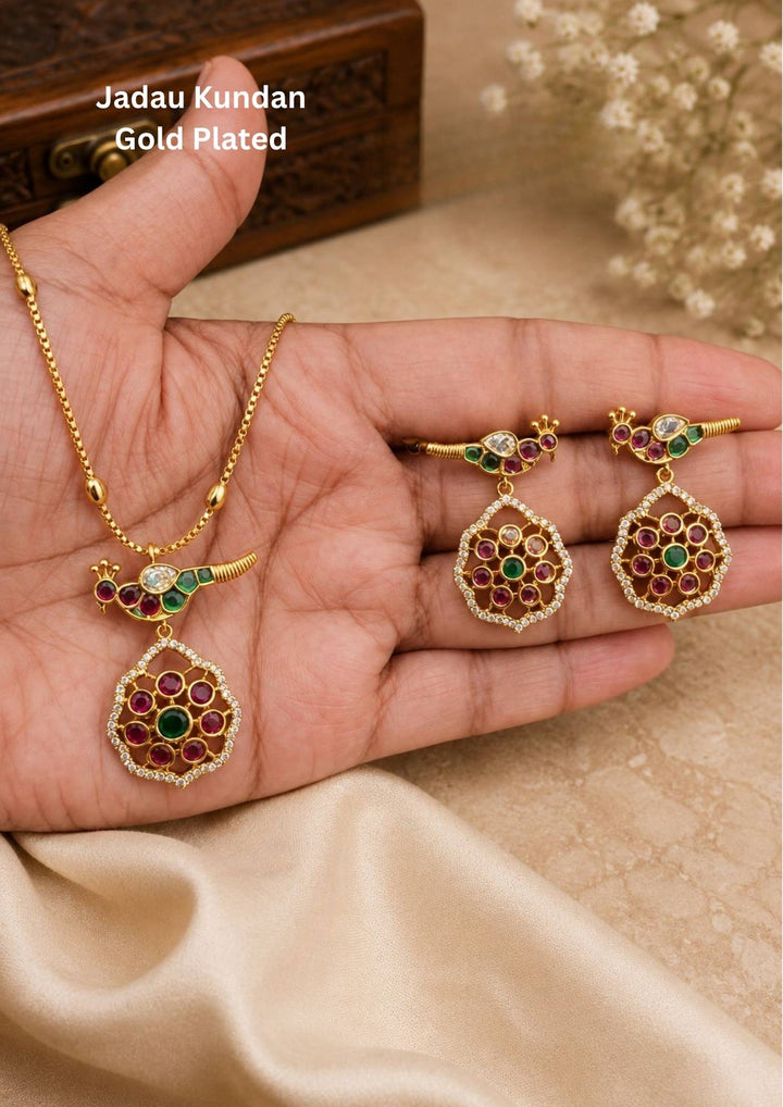 Premium gold plated jewelry set featuring a delicate chain necklace with a floral-inspired central pendant embellished with ruby-colored and green stones, paired with matching drop earrings. Perfect for traditional wear, weddings, festive occasions, parties, and gifting.