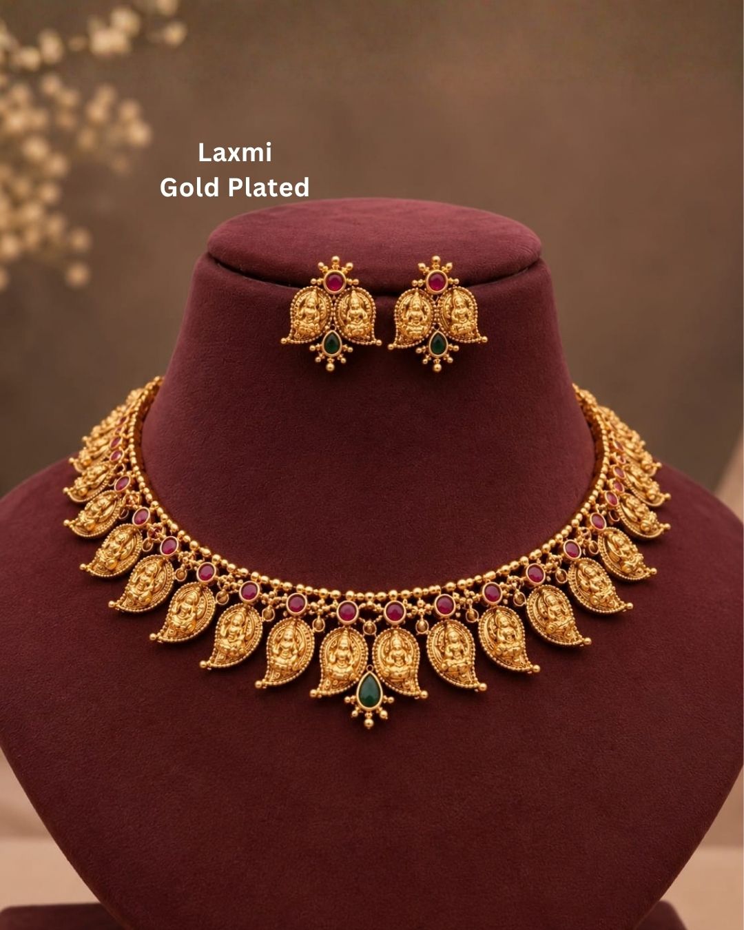 Elegant gold plated Lakshmi Devi necklace set featuring multiple detailed temple motifs, red and green stone embellishments, a central green teardrop pendant, and matching earrings, perfect for festive and traditional occasions.