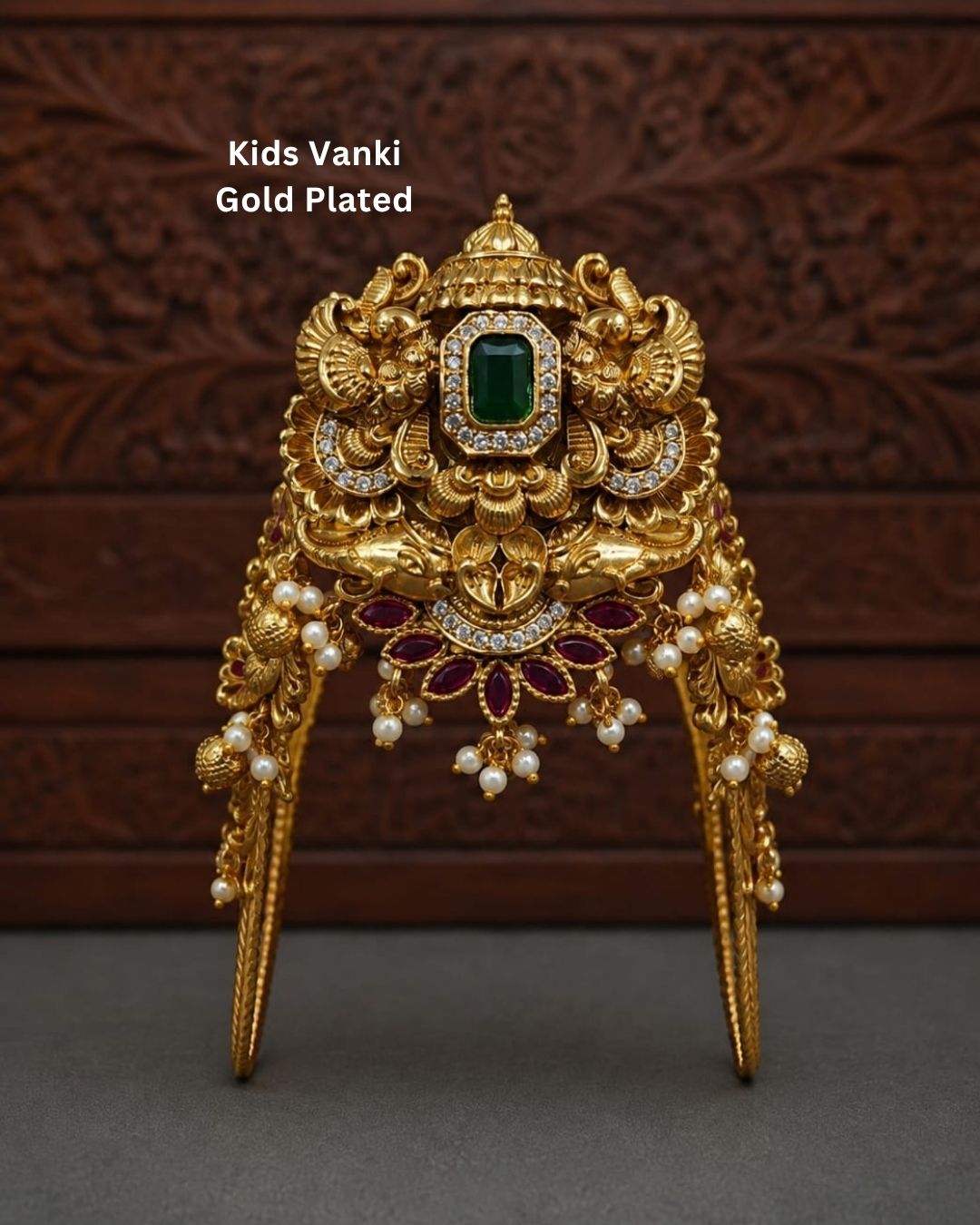 Beautiful gold plated kids vanki featuring an intricately crafted traditional design with a large green stone centerpiece, sparkling clear stones, ruby floral motifs, and elegant pearl drops. Perfect for traditional wear, weddings, festivals, classical dance, special occasions, and gifting.