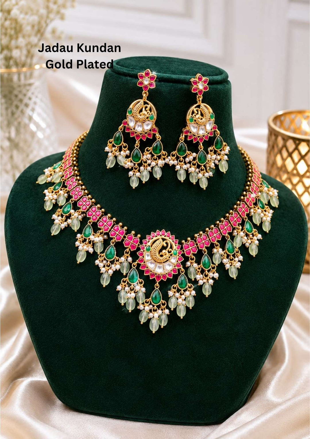 Jadau kundan gold plated royal peacock choker necklace set featuring a wide collar band of pink ruby tiles leading to a grand center medallion with an enamel peacock motif, surrounded by hanging teardrop emerald stones, white pearls, and mint green quartz beads. This luxury statement set is paired with matching large peacock chandelier earrings that provide a rich and classy appearance suitable for weddings, bridal events, receptions, major festivals with skin friendly quality