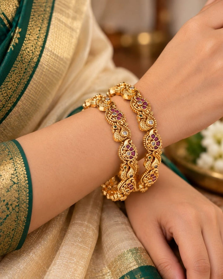 Jadau kundan gold plated bangles featuring intricate peacock motifs, purple and green stone accents, and antique gold detailing.