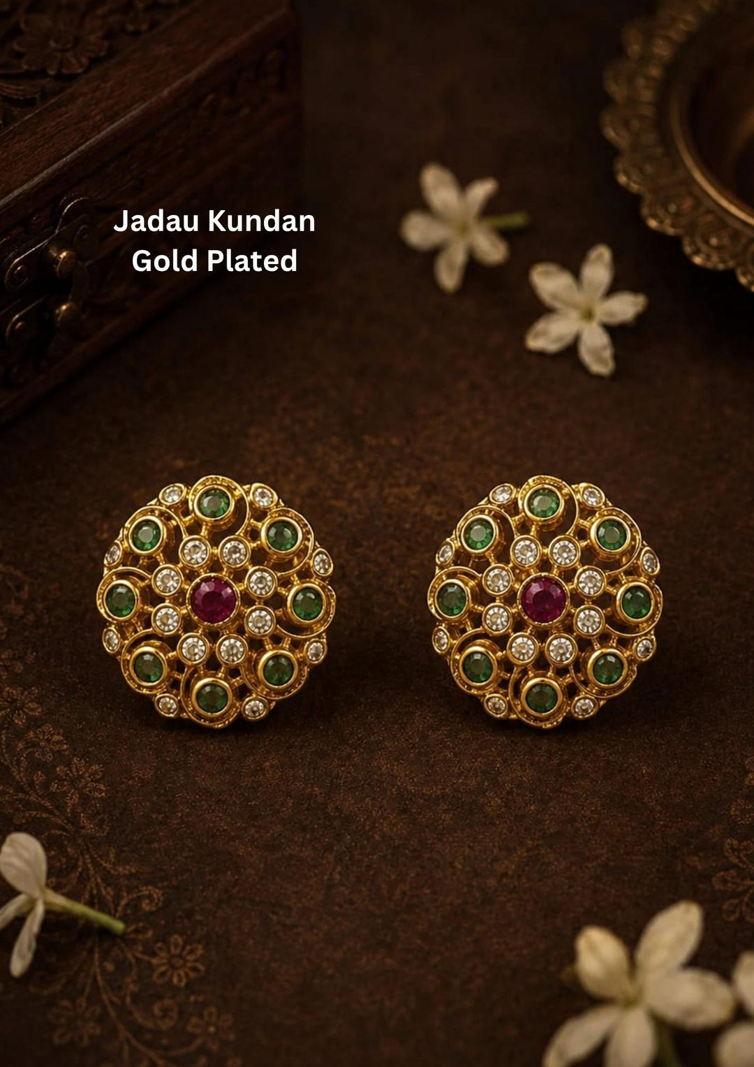 Traditional jadau kundan gold plated stud earrings featuring an intricate circular floral design crafted with radiant emerald-colored stones, sparkling kundan stones and a striking pink center stone. The symmetrical pattern and antique-inspired craftsmanship create a rich ethnic appeal suitable for weddings, festivals, poojas and traditional celebrations.