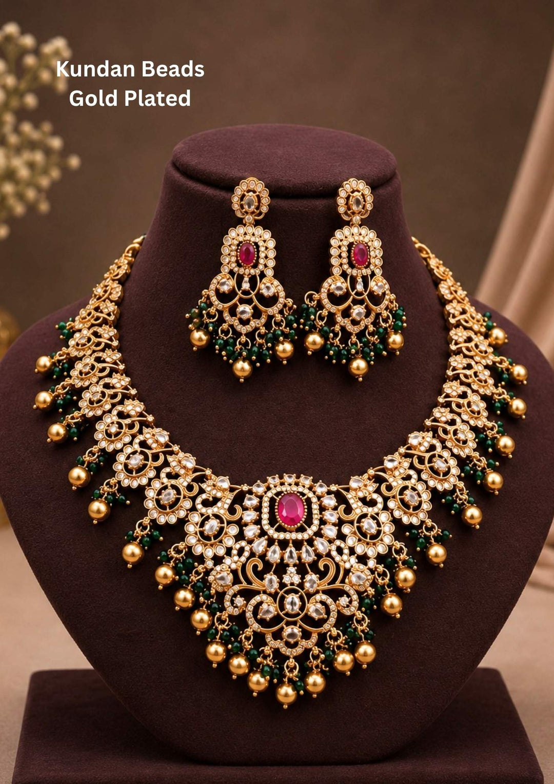 Traditional Kundan Beads gold plated heavy bridal necklace and matching long earrings The grand neckpiece features a wide, intricate central bib pattern heavily encrusted with white Kundan stones, highlighted by a large oval ruby pink gemstone in the middle. The entire lower border of the necklace and matching drop earrings is decorated with clusters of dark green beads and hanging golden balls (ghungroo drops).