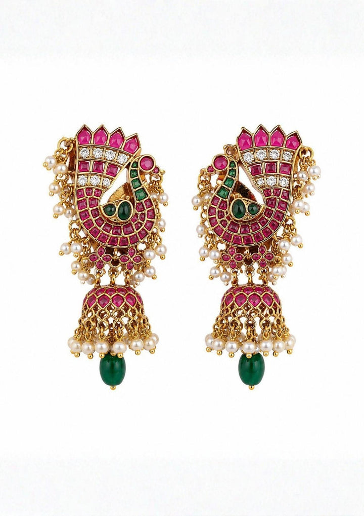 Jadau kundan gold plated jhumka earrings featuring an intricate peacock motif studded with pink ruby stones, green stone accents, and clear kundan detailing. These lightweight traditional earrings are crafted with a classic dome-shaped jhumka