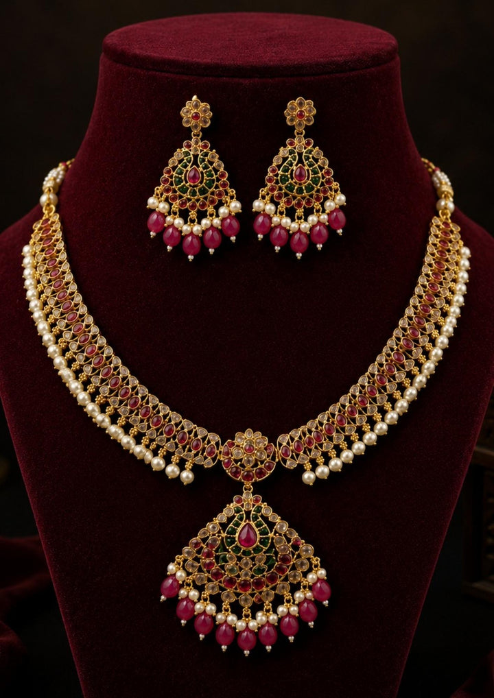 Beautiful Jadau Kundan gold plated pearl pendant necklace set featuring ruby and green stones, intricate kundan craftsmanship, pearl accents, and matching earrings. Perfect for weddings, festivals, temple visits, traditional outfits, bridal wear, and premium gifting.