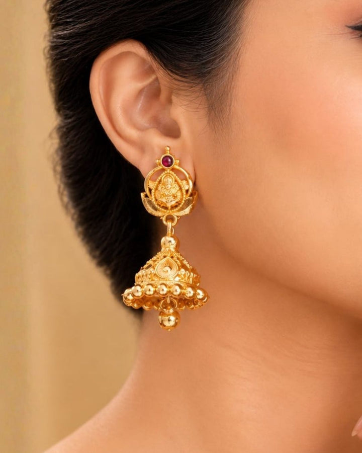 Beautiful traditional gold plated Lakshmi jhumka earrings featuring intricate temple-inspired craftsmanship, red stone detailing, ornate floral patterns, and hanging gold beads. Perfect for sarees, festive occasions, weddings, and traditional events.