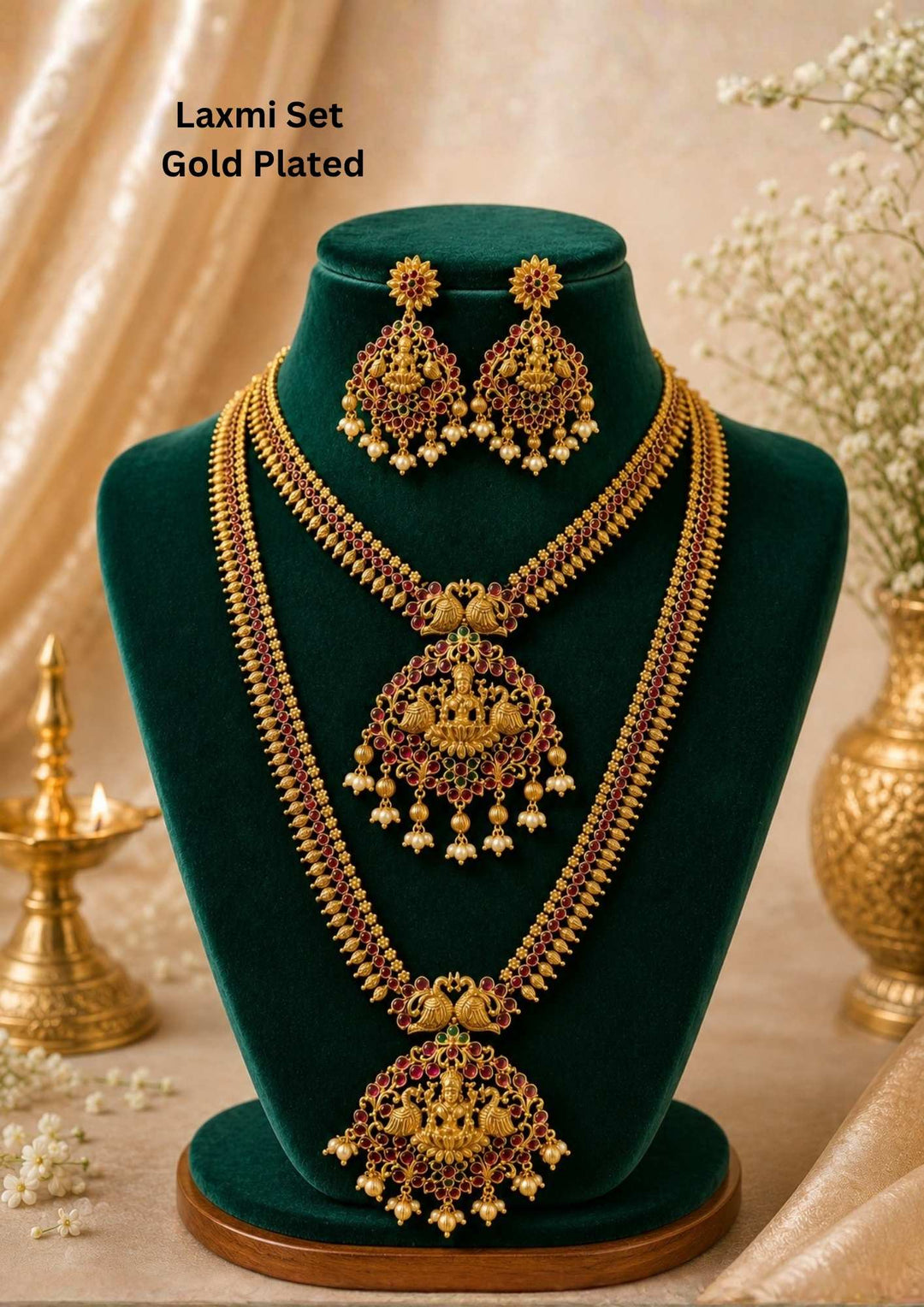 Traditional South Indian temple jewelry set featuring two layered gold plated necklaces adorned with Goddess Lakshmi motifs, ruby-colored stones and pearl danglers. The matching statement earrings complete this grand bridal jewelry collection.