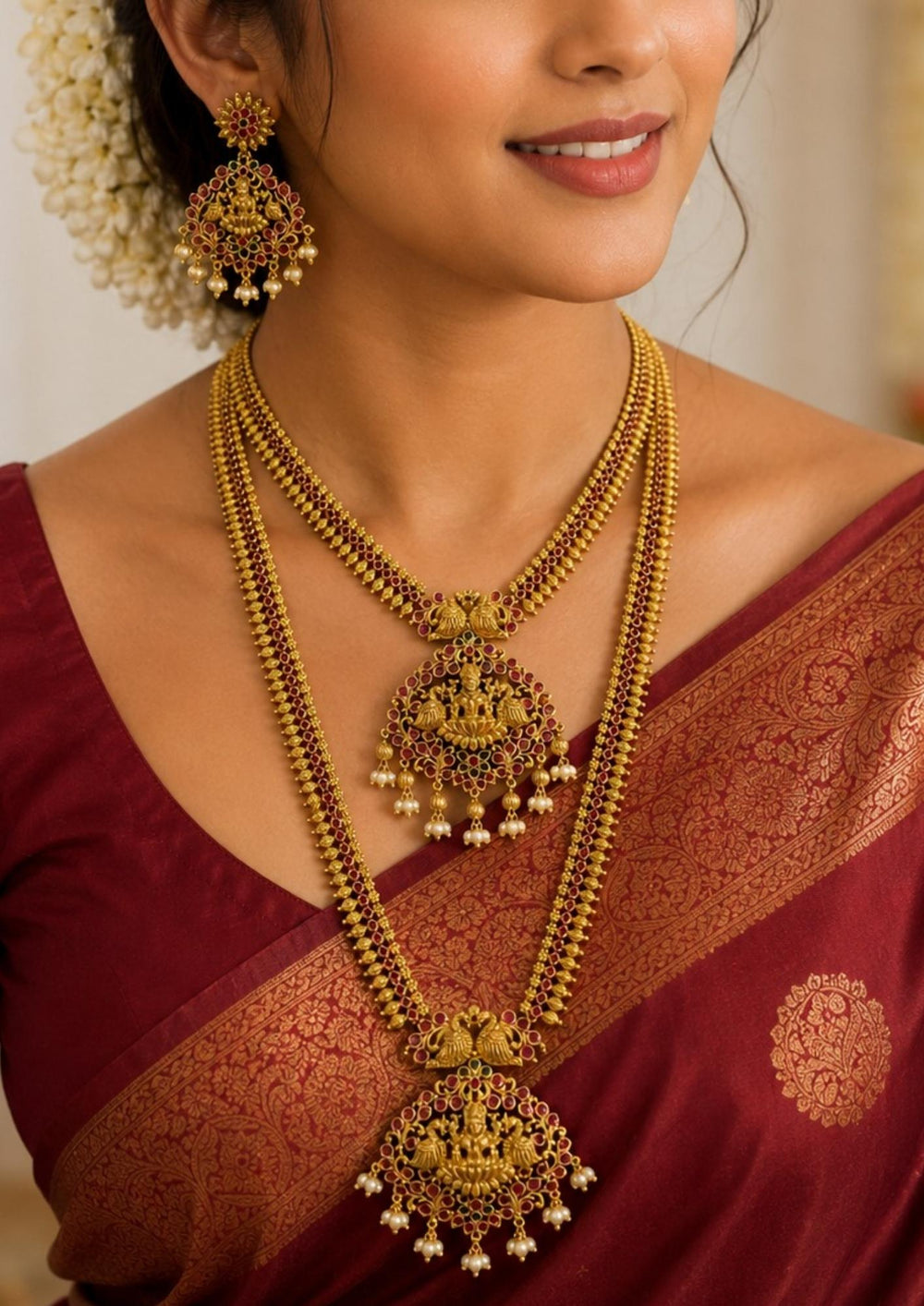 South indian women wearing a Traditional South Indian temple jewelry set featuring two layered gold plated necklaces adorned with Goddess Lakshmi motifs, ruby-colored stones and pearl danglers. The matching statement earrings complete this grand bridal jewelry collection.