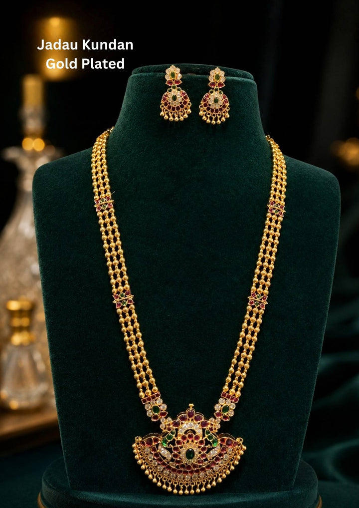 Elegant jadau kundan gold plated long haram necklace set featuring multiple strands of gold beads paired with an intricately designed kundan pendant embellished with ruby and emerald-tone stones. The matching earrings complete the traditional bridal look with rich ethnic detailing.